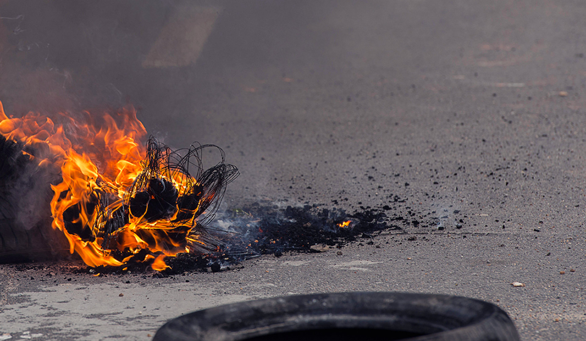 A tire ignited and burning on the ground, positioned adjacent to an unburned tire.