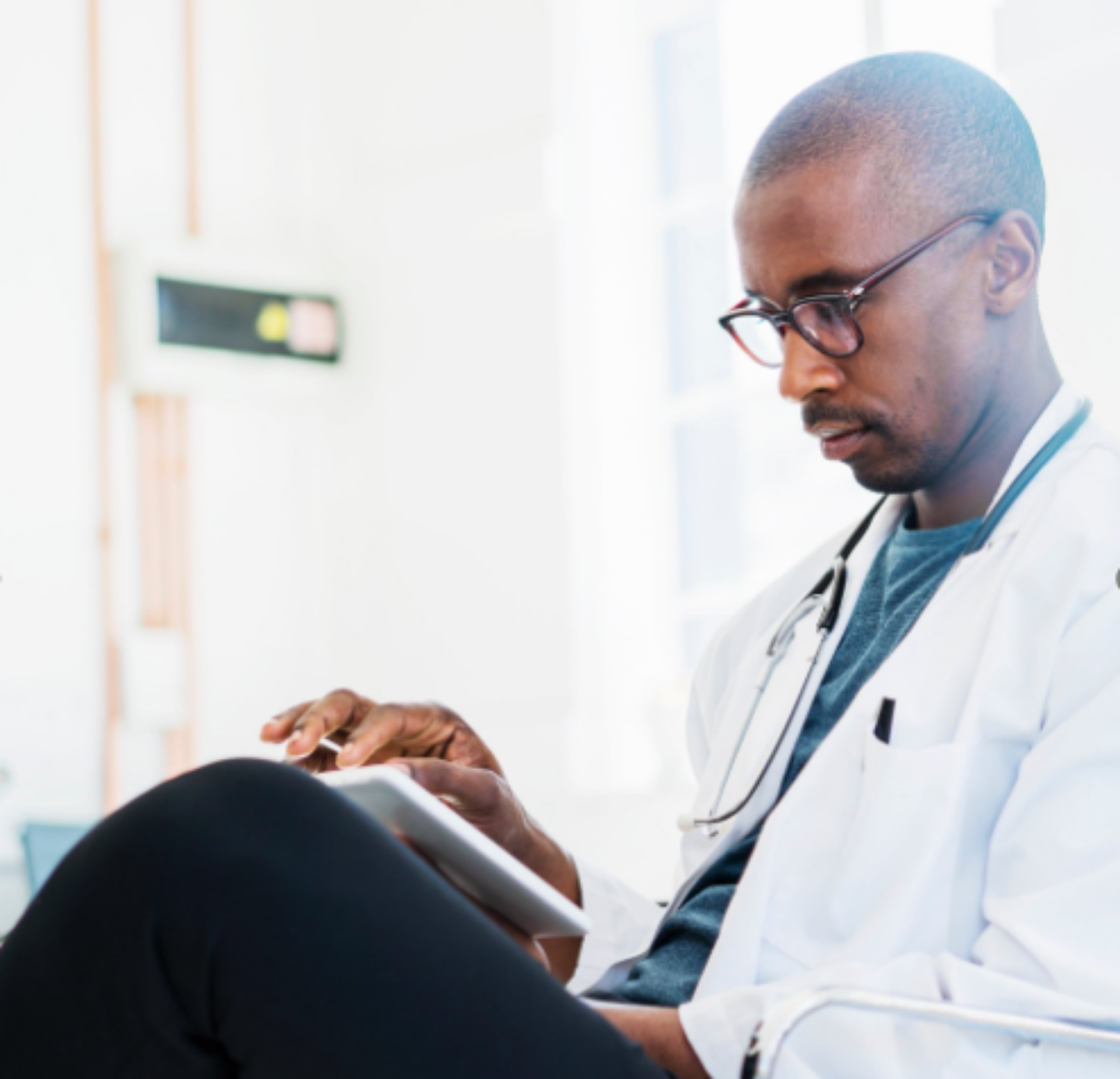 A male doctor dressed in a white coat, sitting on a chair, symbolizing care and expertise in a medical setting.