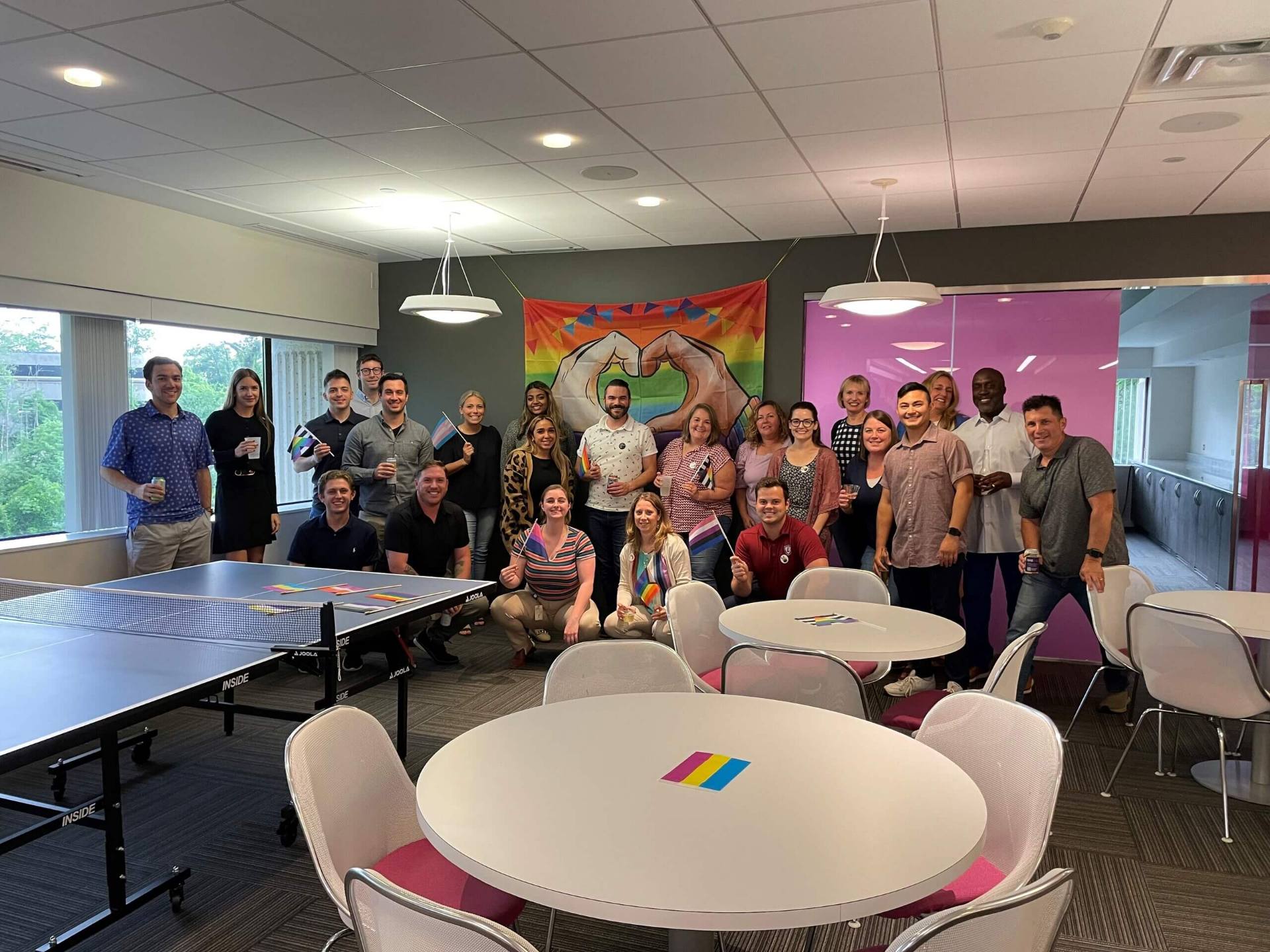 A group of individuals smiling and posing together in front of a ping pong table, capturing a moment of celebrating pride.