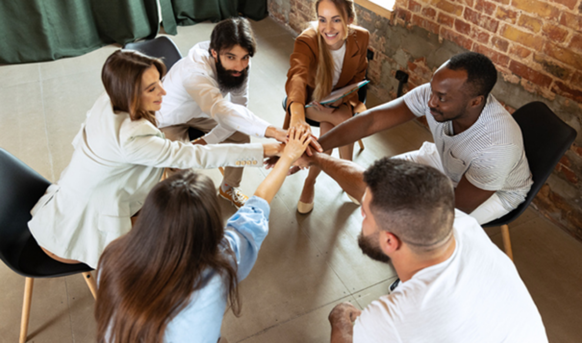 A diverse group of individuals seated at a table, enthusiastically raising their hands in a collaborative discussion.