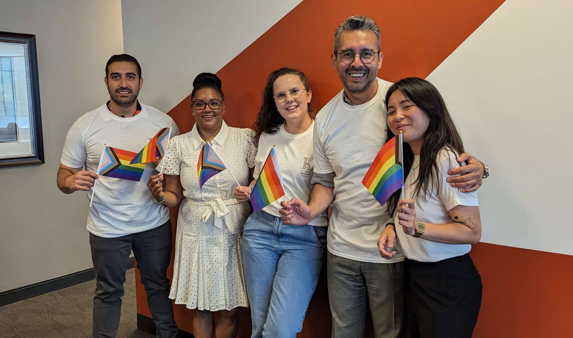 A team of proud colleagues standing together, smiling for a group photo in a well-lit office environment.