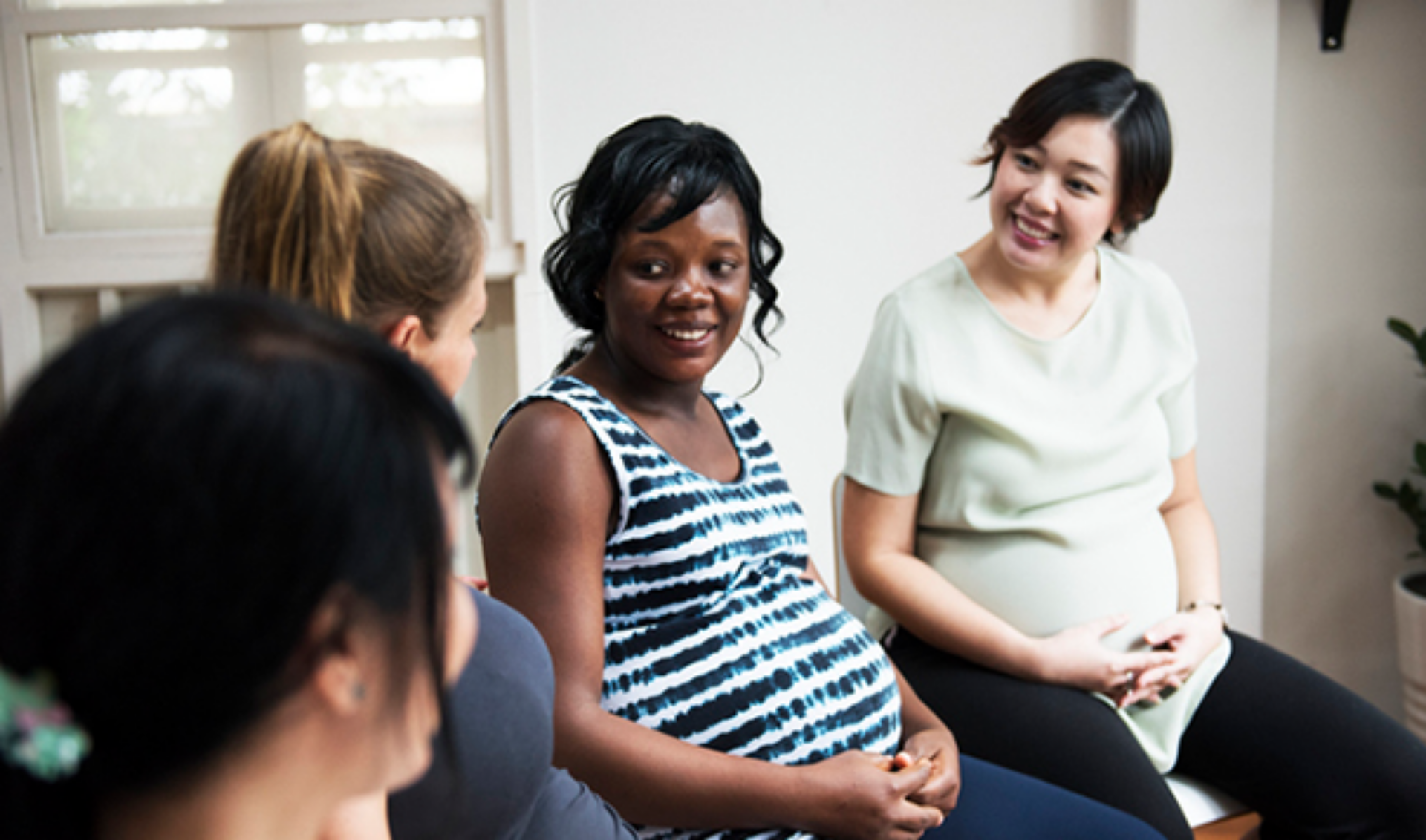 A diverse group of pregnant women seated together, engaged in conversation and enjoying each other's company.