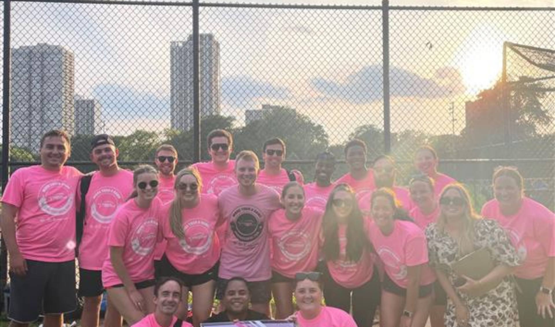 A group of individuals wearing pink shirts smiles and poses together for a photograph.