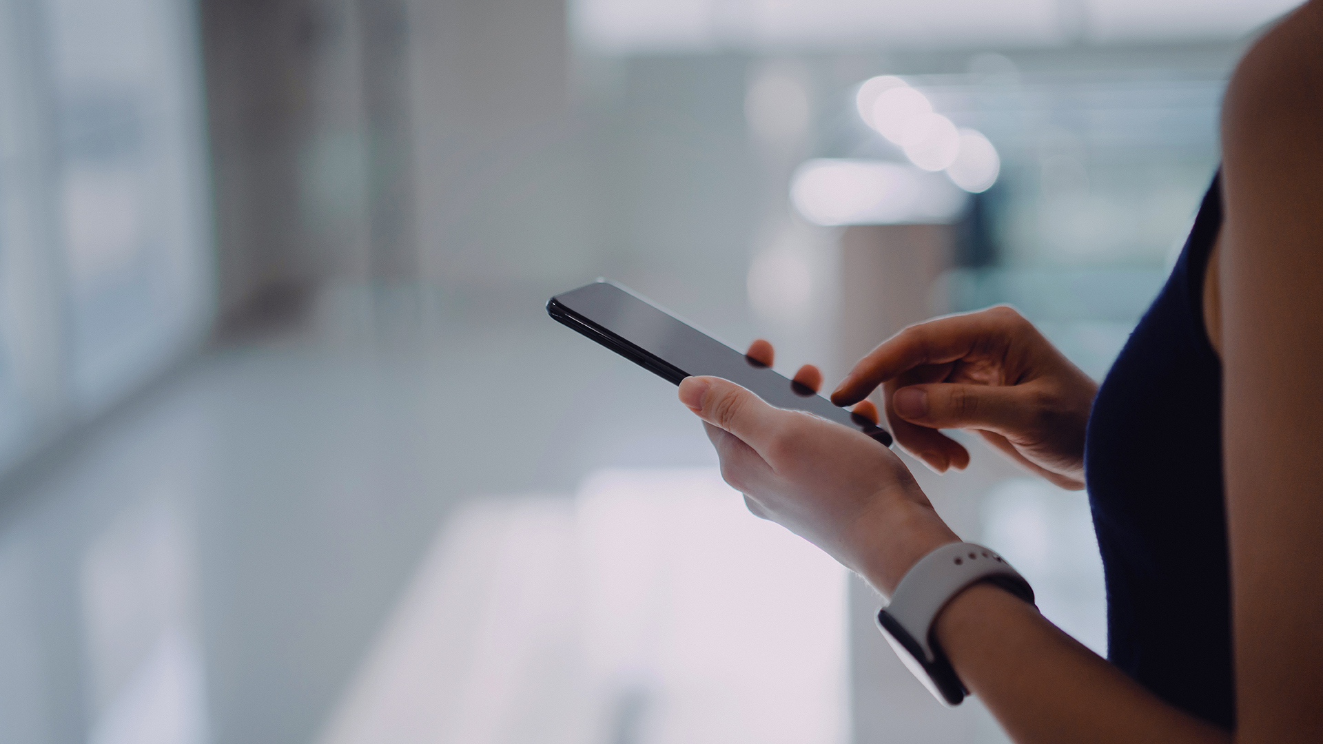 A woman with a smartphone in her hand, appearing focused as she interacts with the device.