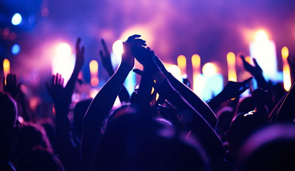 An energetic audience at a concert, with many individuals lifting their hands in celebration and enjoyment.