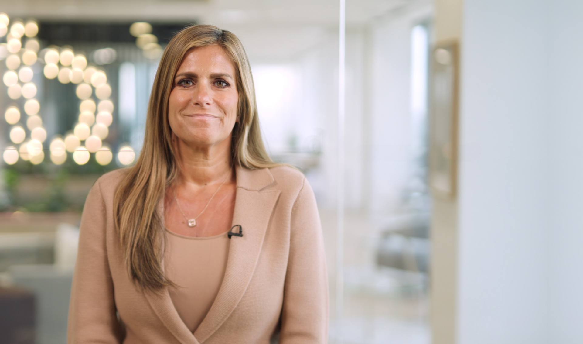 A woman dressed in a business suit stands by a window, exuding professionalism and determination in a corporate setting.