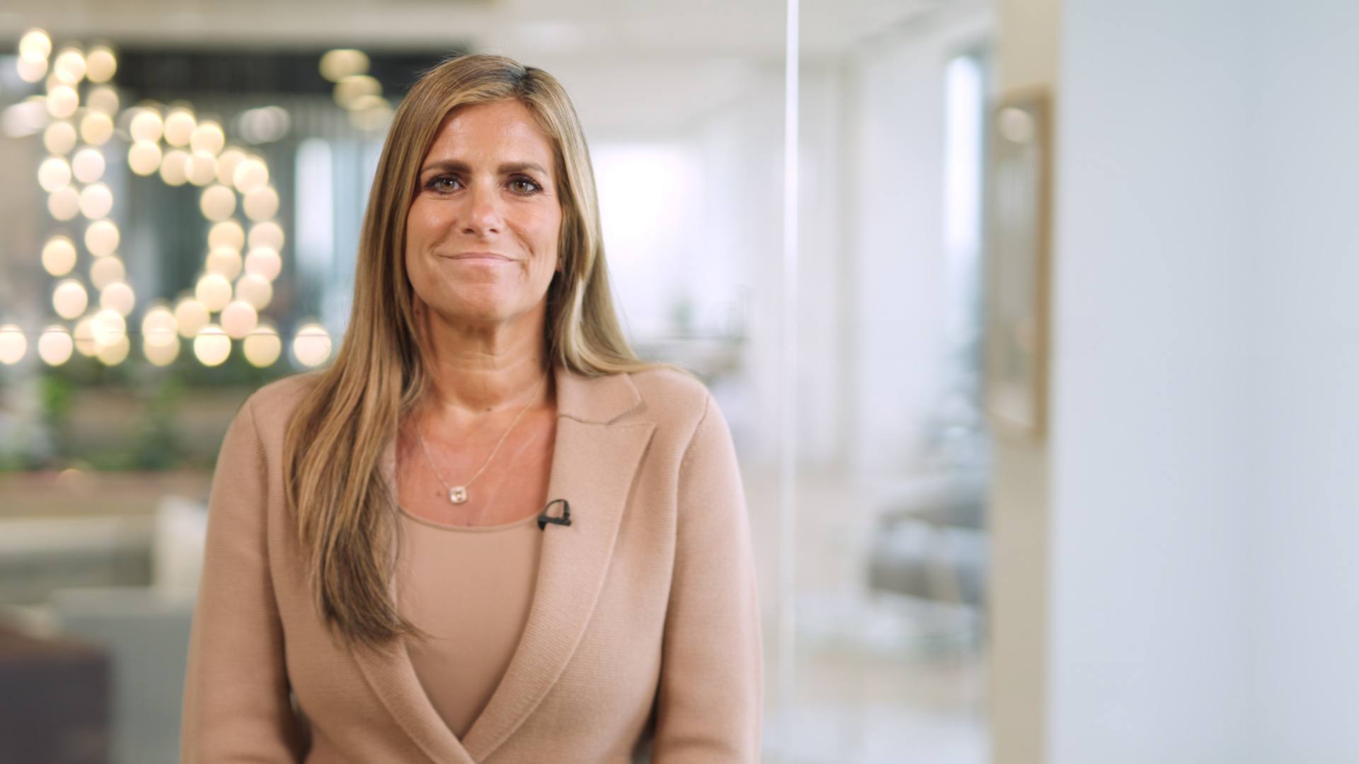 A woman dressed in a business suit stands by a window, exuding professionalism and determination in a corporate setting.