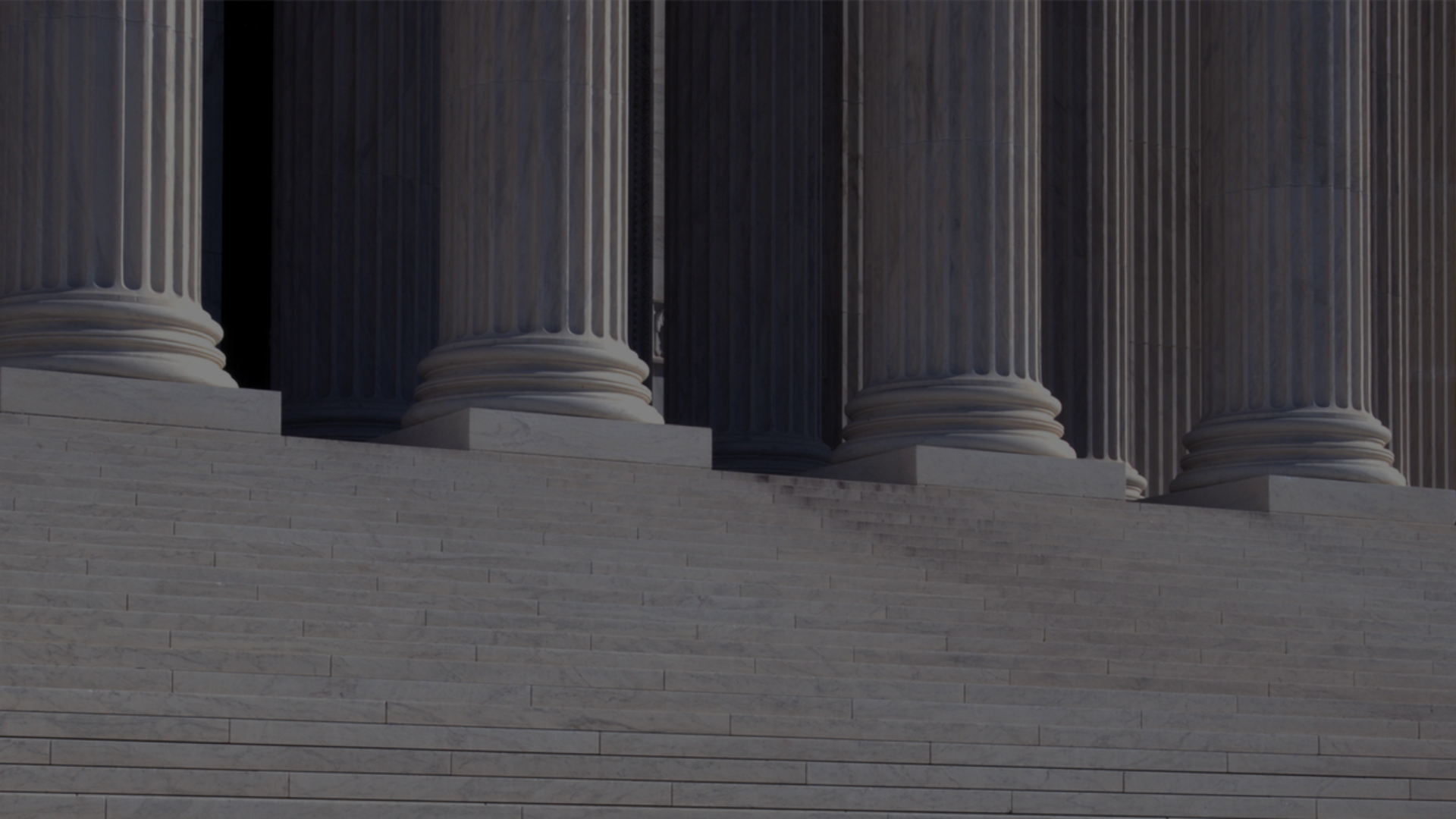 A man walks down the steps of a neo-classical building, surrounded by impressive columns that define its architectural style.