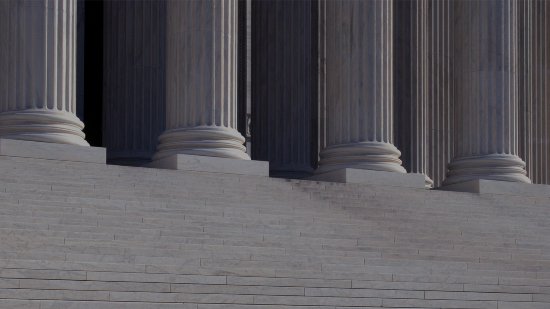 A man walks down the steps of a neo-classical building, surrounded by impressive columns that define its architectural style.