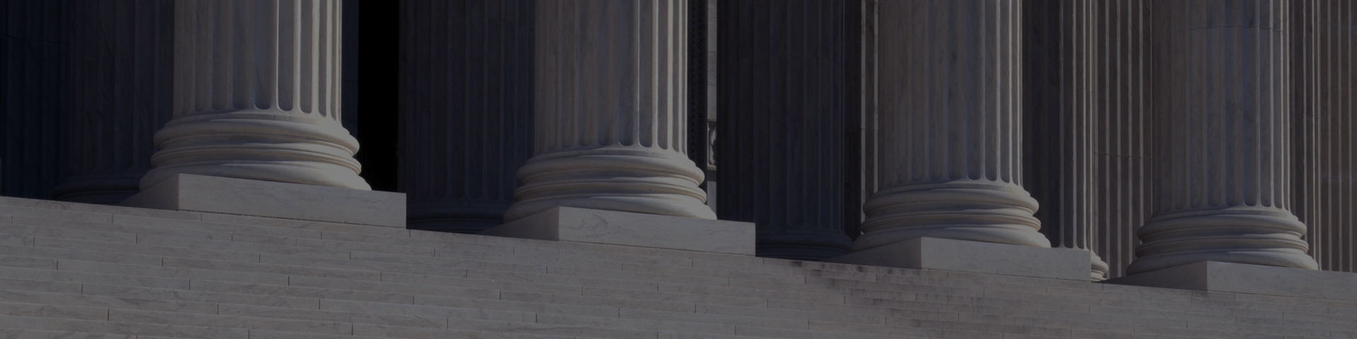A man walks down the steps of a neo-classical building, surrounded by impressive columns that define its architectural style.