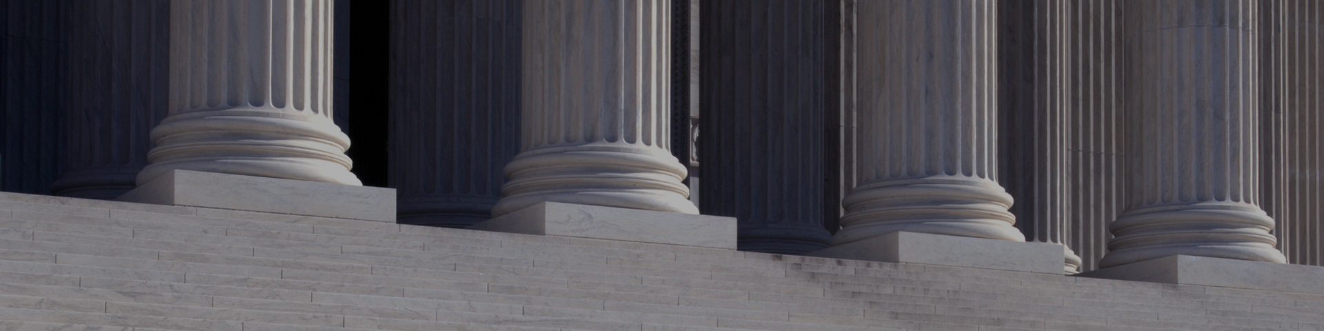 A man walks down the steps of a neo-classical building, surrounded by impressive columns that define its architectural style.