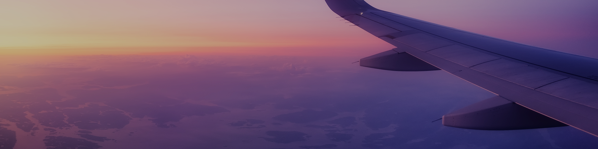The wing of an airplane silhouetted against a vibrant sunset, showcasing a blend of orange and purple skies.