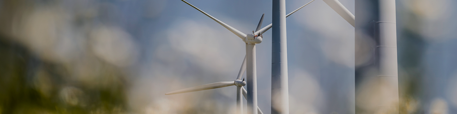A close-up view of a wind turbine against a clear blue sky, showcasing its blades and structure in detail.