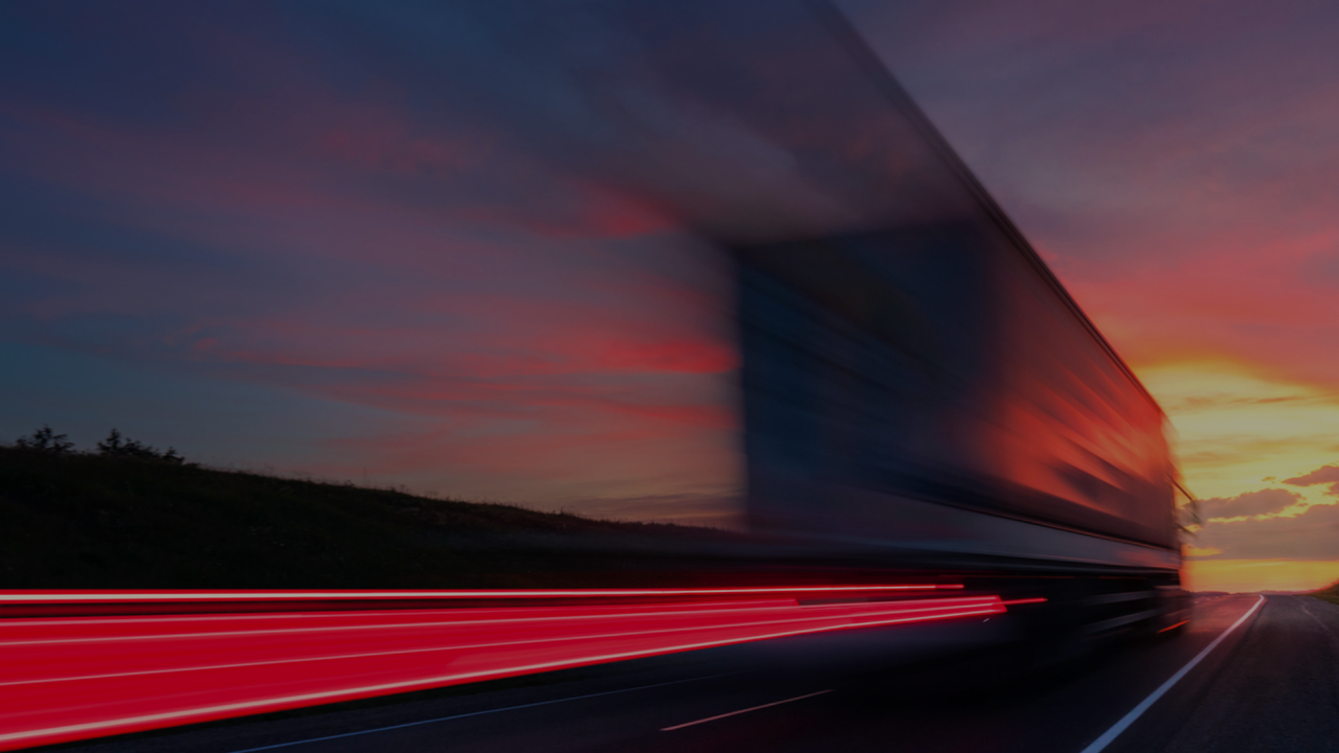 A truck moves down a highway, with a picturesque sunset casting warm hues across the scene.
