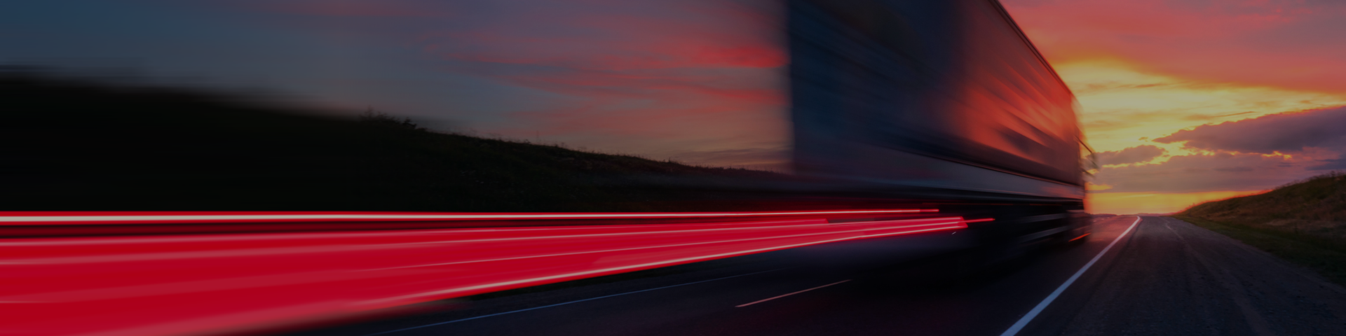 A truck moves down a highway, with a picturesque sunset casting warm hues across the scene.