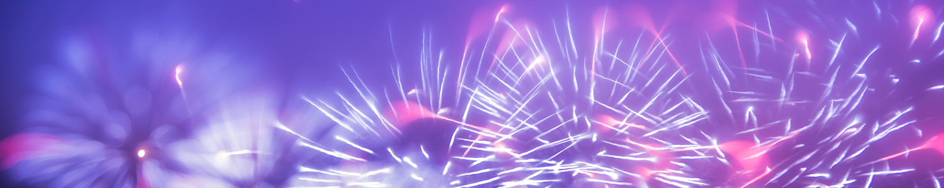 Fireworks explode in brilliant colors against the night sky, with trees providing a natural backdrop.