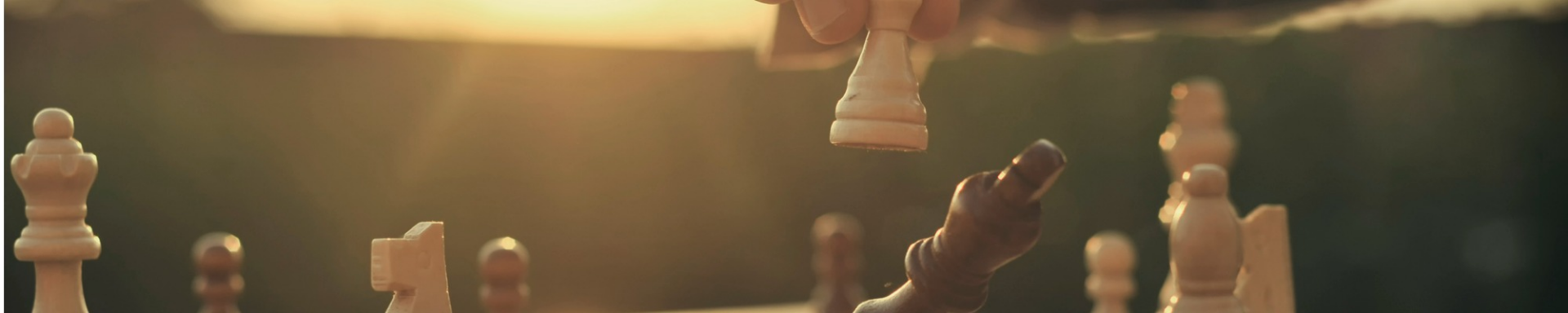 An individual playing chess, strategically positioning wooden pieces on a traditional chessboard, against the backdrop of a warm sunset.
