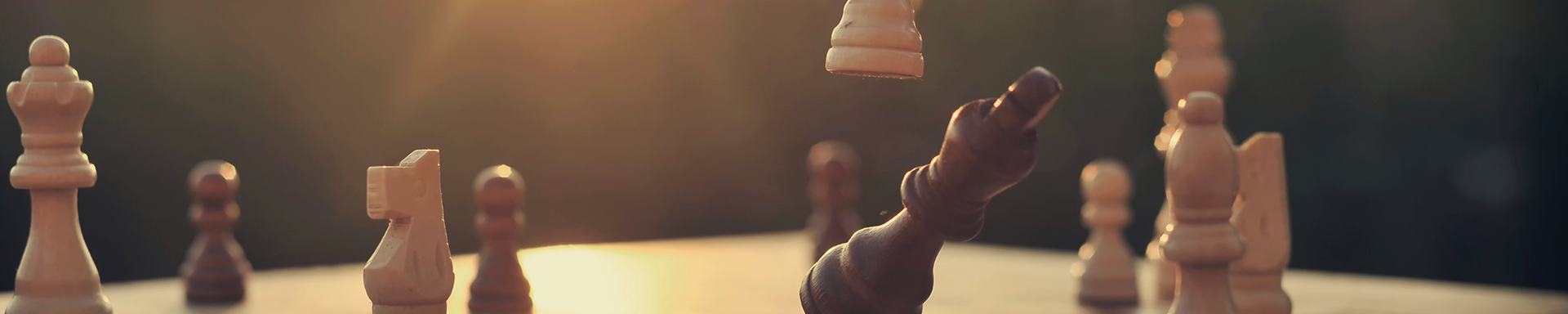 An individual playing chess, strategically positioning wooden pieces on a traditional chessboard, against the backdrop of a warm sunset.