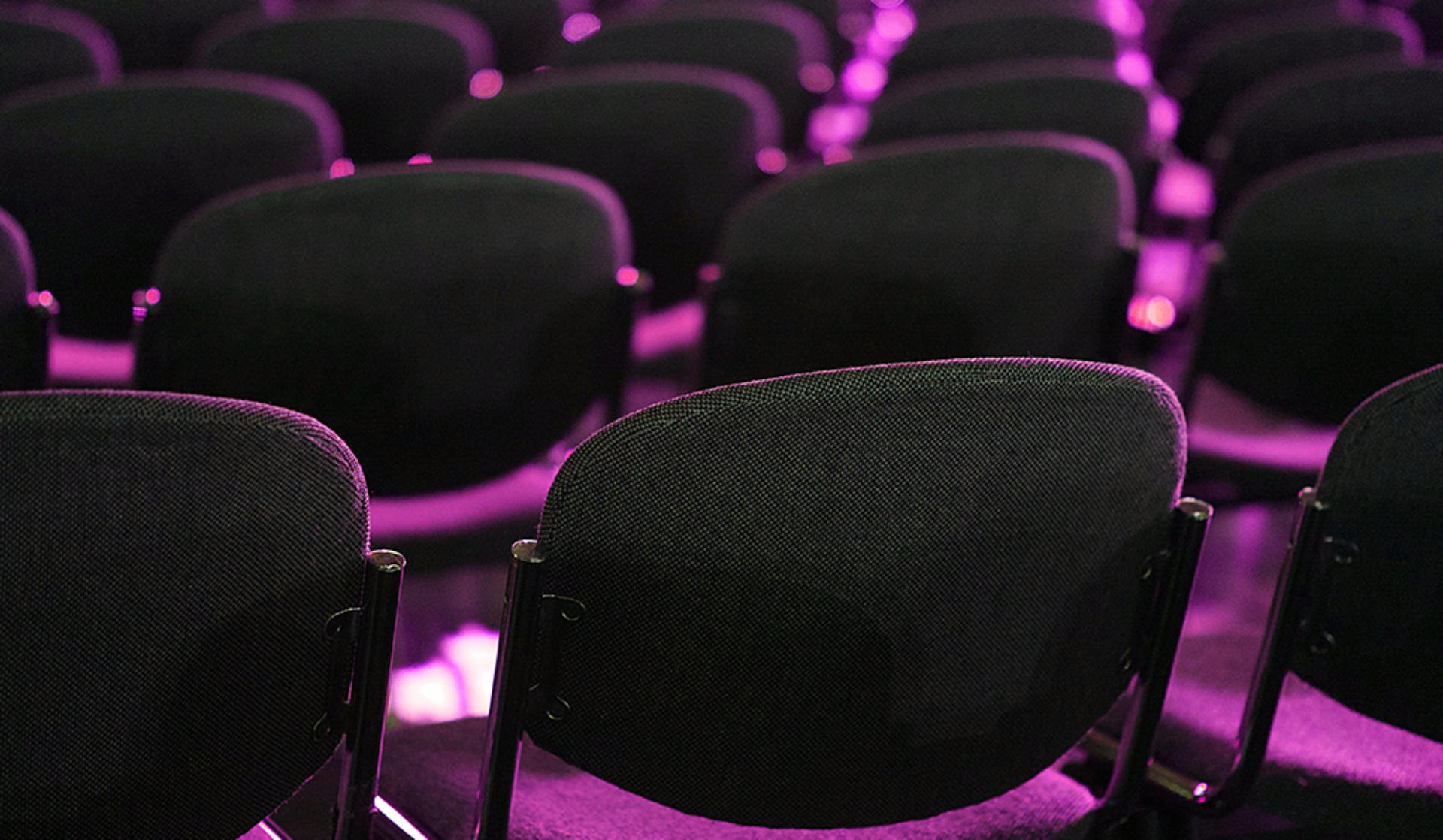 A series of chairs positioned in a darkened event space, evoking a sense of stillness and solitude.